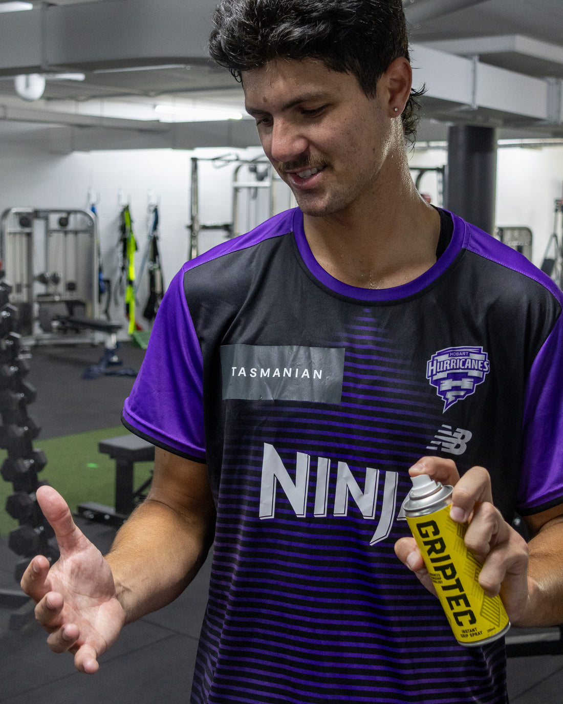 Athlete spraying Griptec Instant Grip Spray onto his hands in the gym
